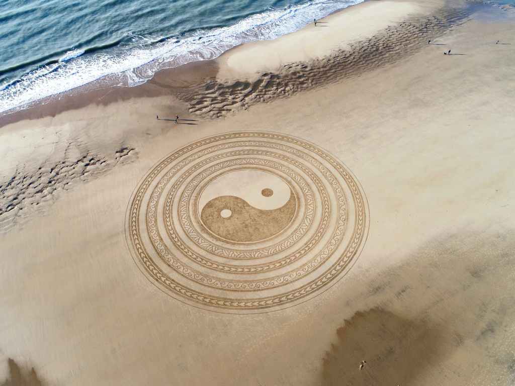 Yin yang symbol encarved on a white sandy beach by the ocean